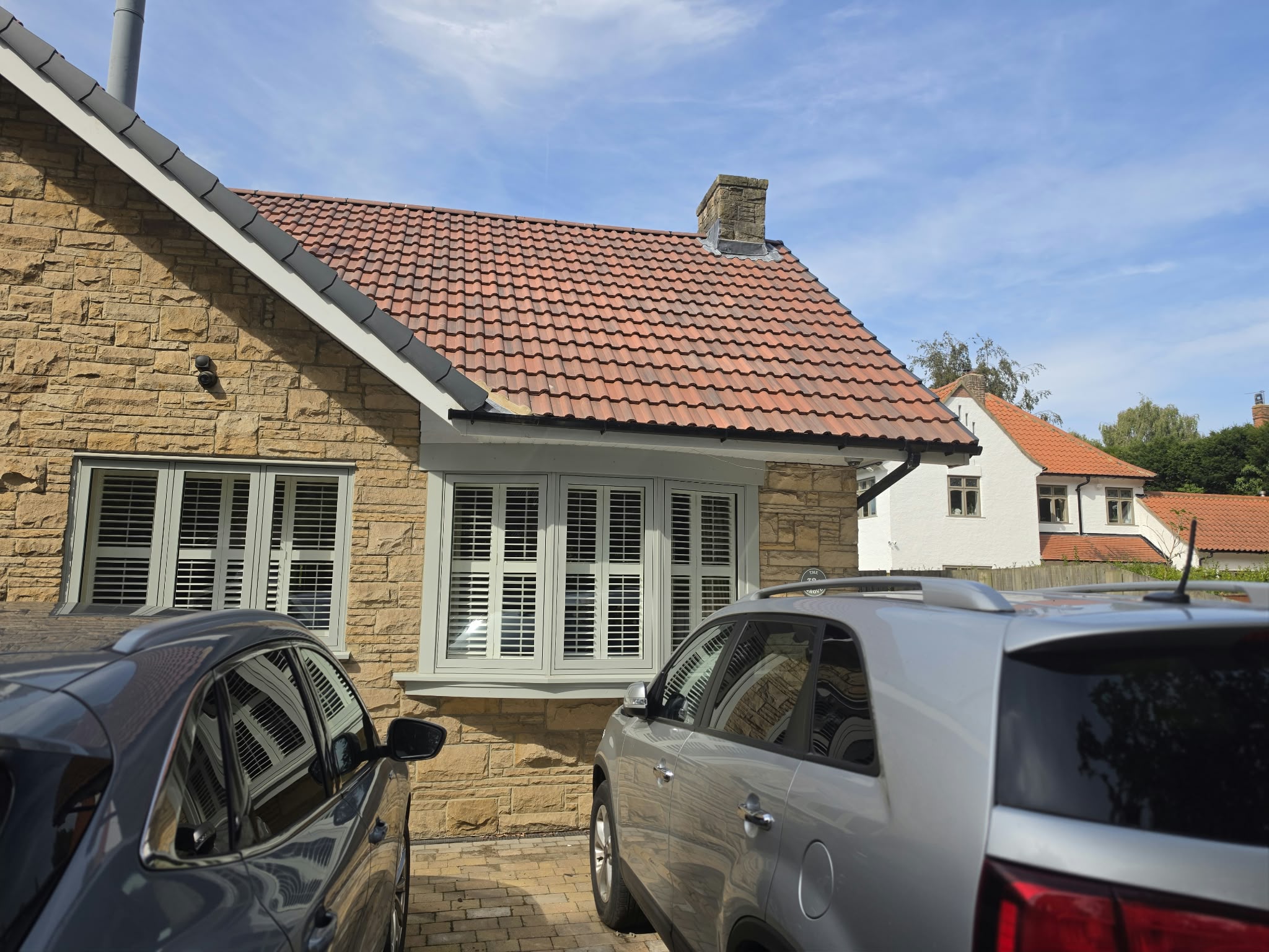 Bay window with shutters, fascia and guttering on a stone house, seen past parked cars